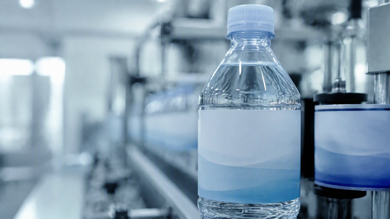 Transparent PET bottle running through a high-speed labeling line, showing the shoulder and the label